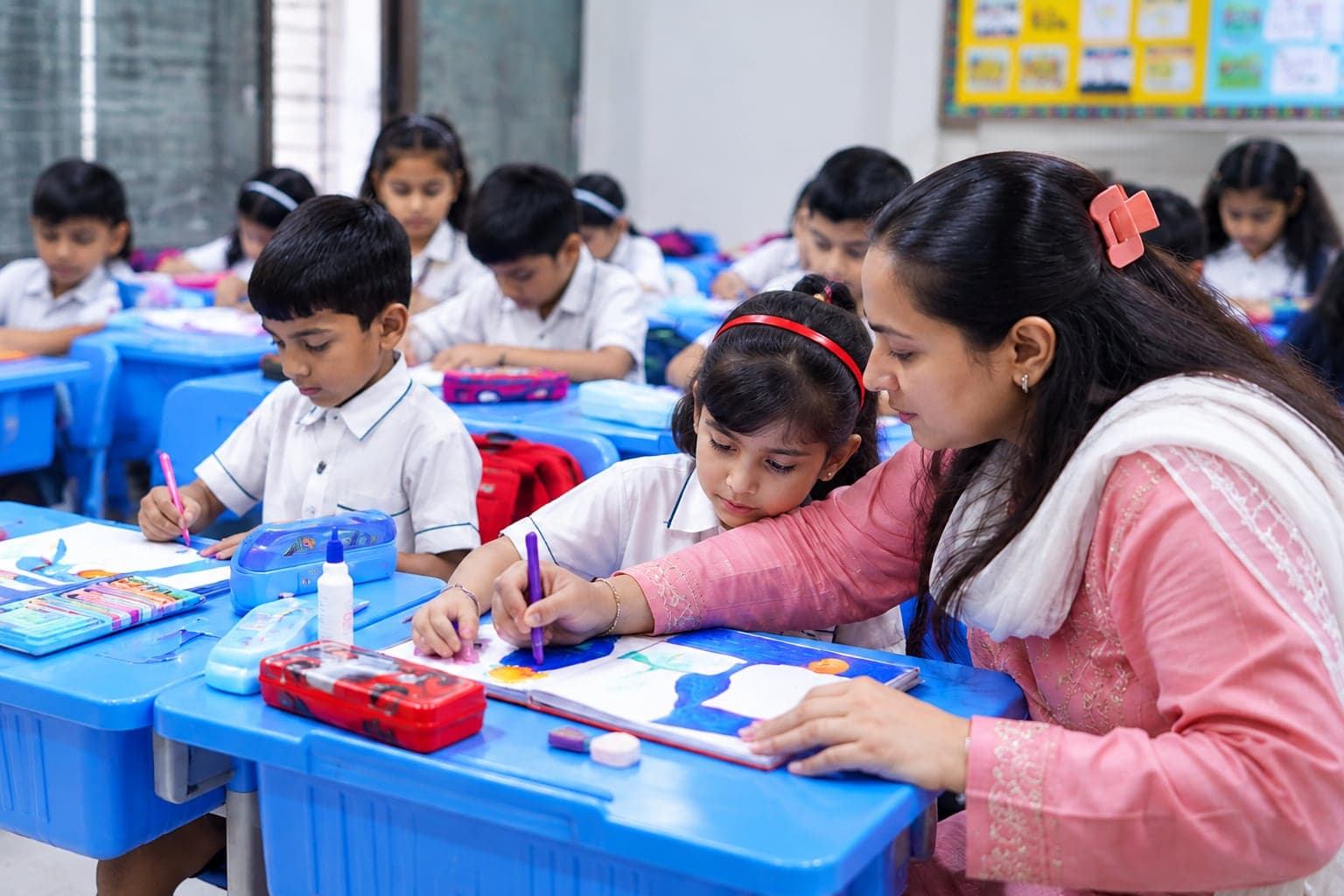 A teacher helping young students with their drawing at their desks