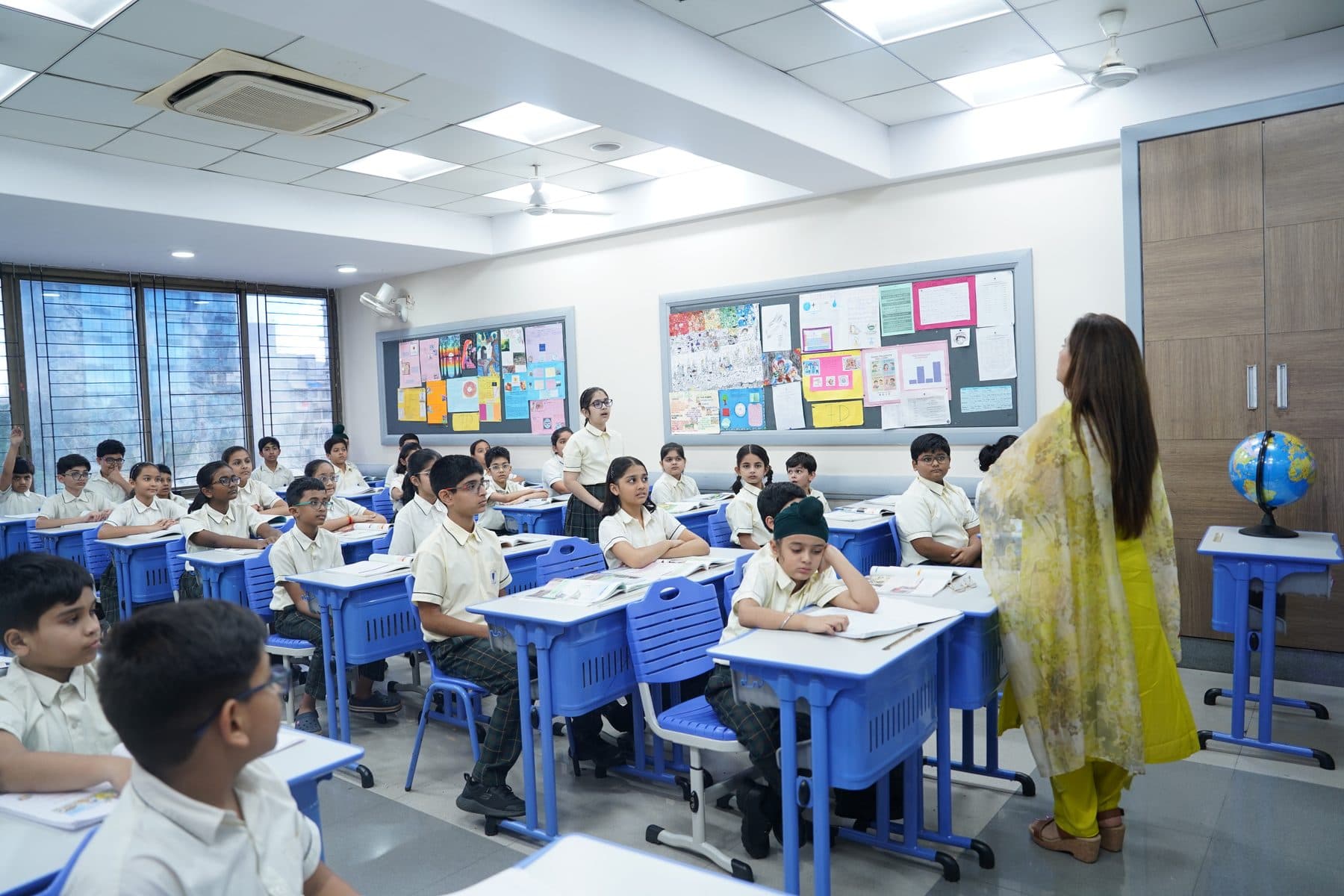 A teacher with a smiling classroom of students raising their hands
